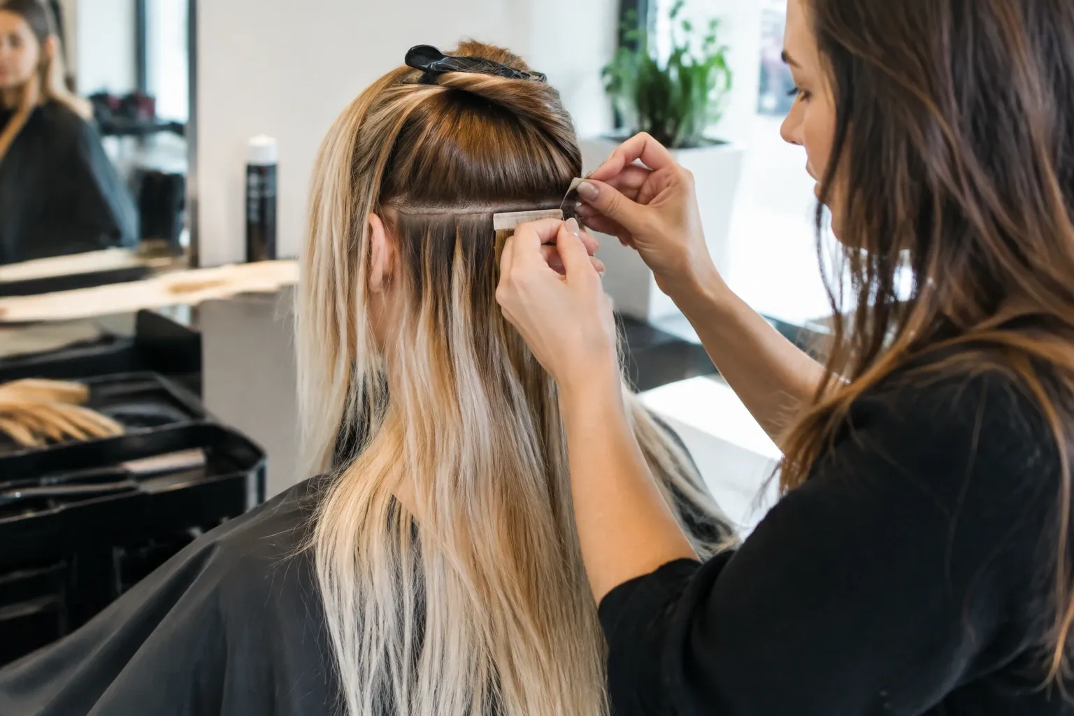 Kapster bevestigt tape-in hairextensions in blond haar bij salonstoel