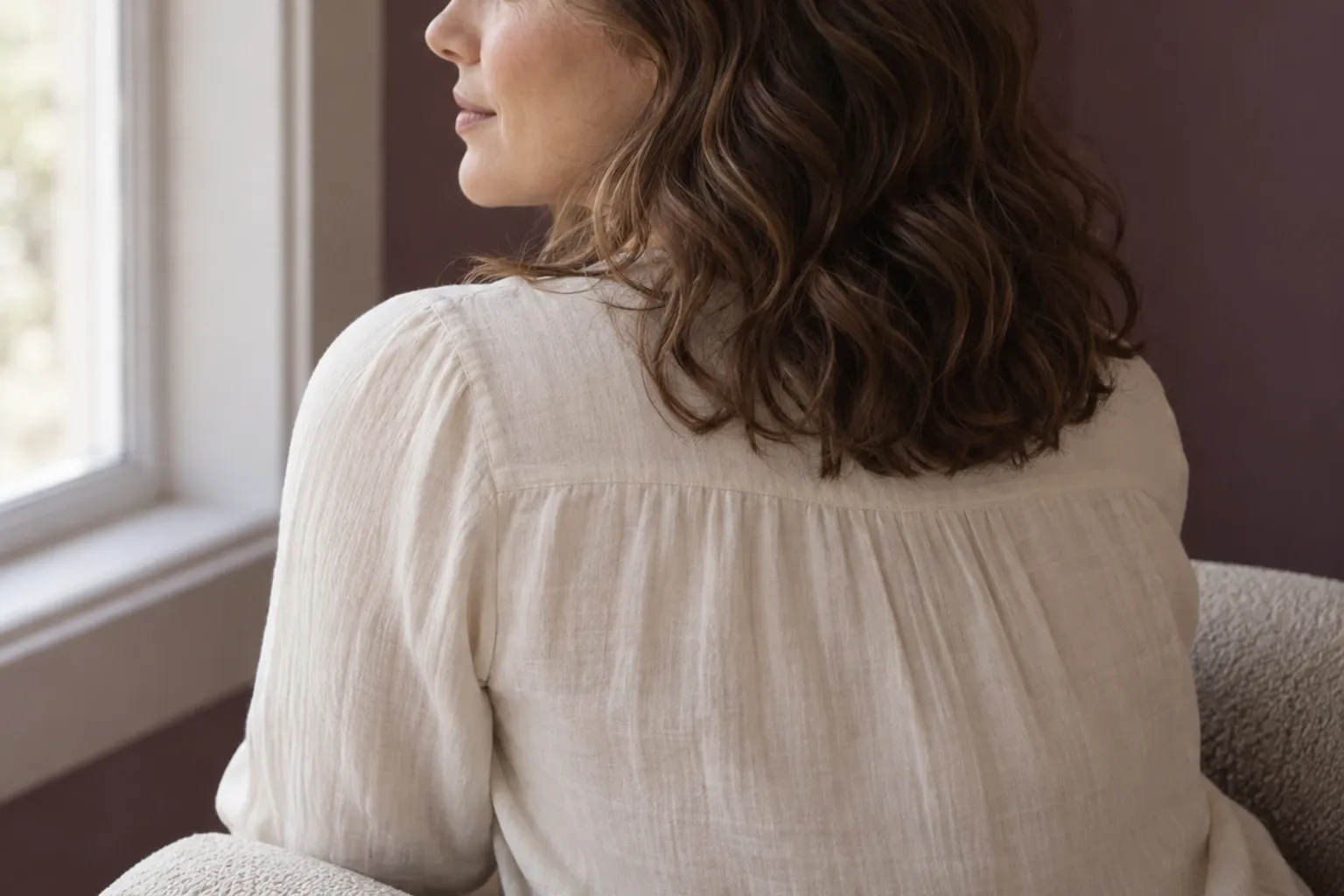 Vrouw met halflang golvend bruin haar zittend bij raam, zachte natuurlijk licht